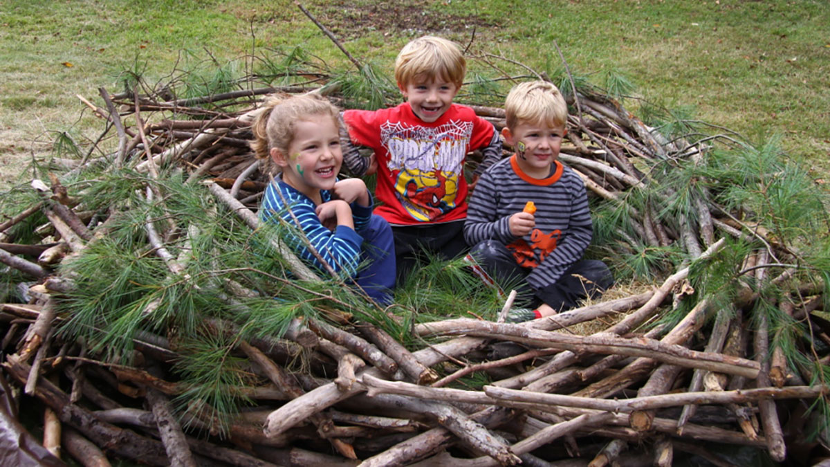 Three smiling kids sitting inside an eagle's nest on the ground.