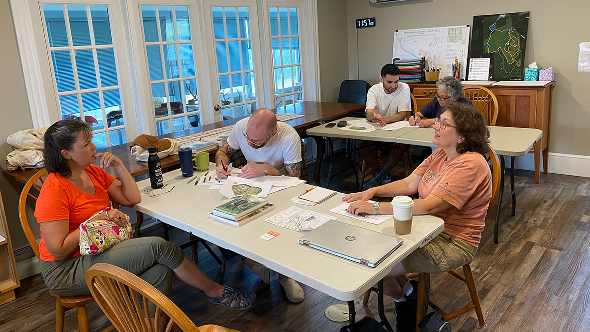 Attendees at a permaculture design workshop at the Van Scott Nature Reserve sit at tables, working on their own design plans.