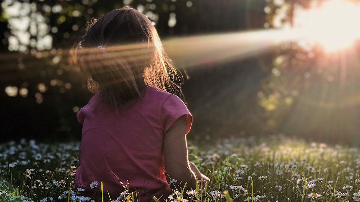 A child sits in the grass at sunset