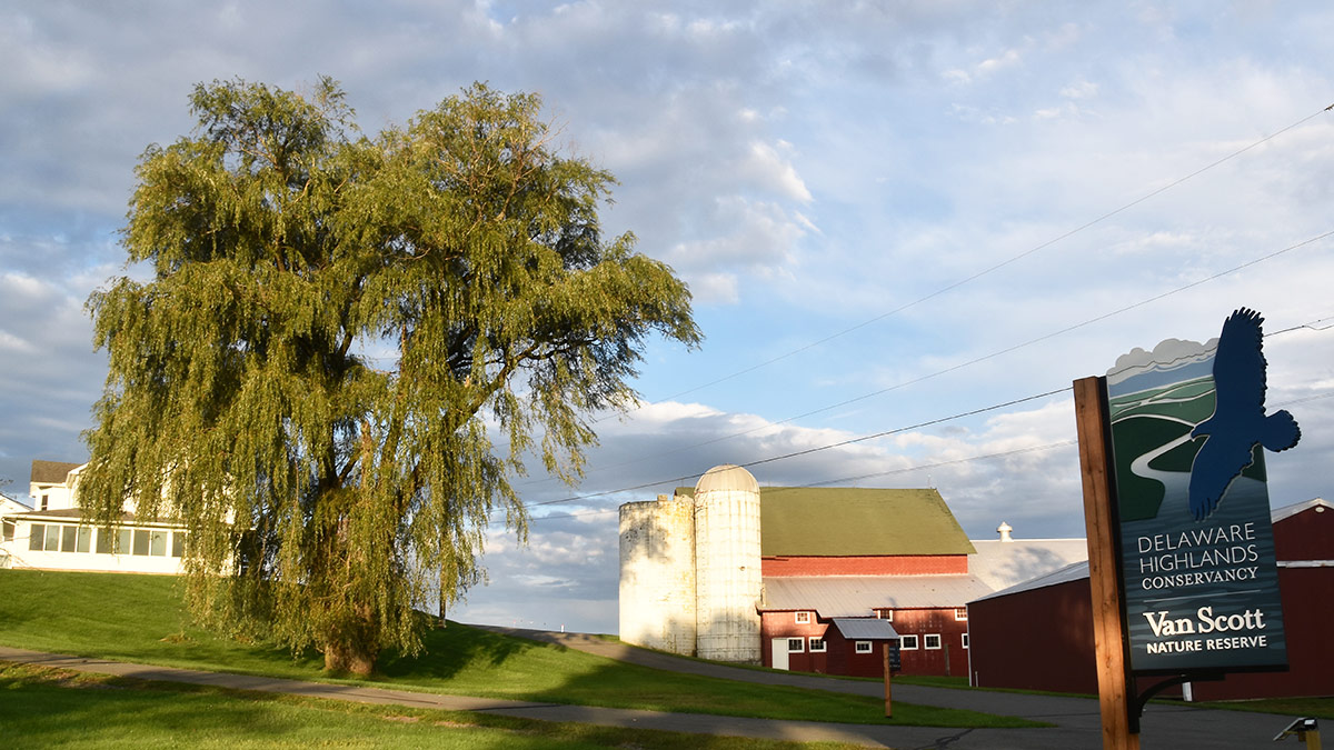 The entrance of the Van Scott Nature Reserve with a sign, red barn and silos, and the farmhouse that is the office headquarters.