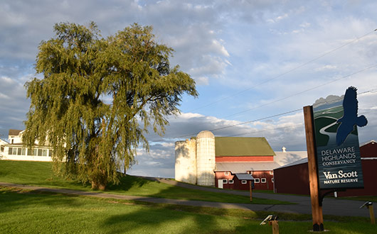 The entrance of the Van Scott Nature Reserve with a sign, red barn and silos, and the farmhouse that is the office headquarters.